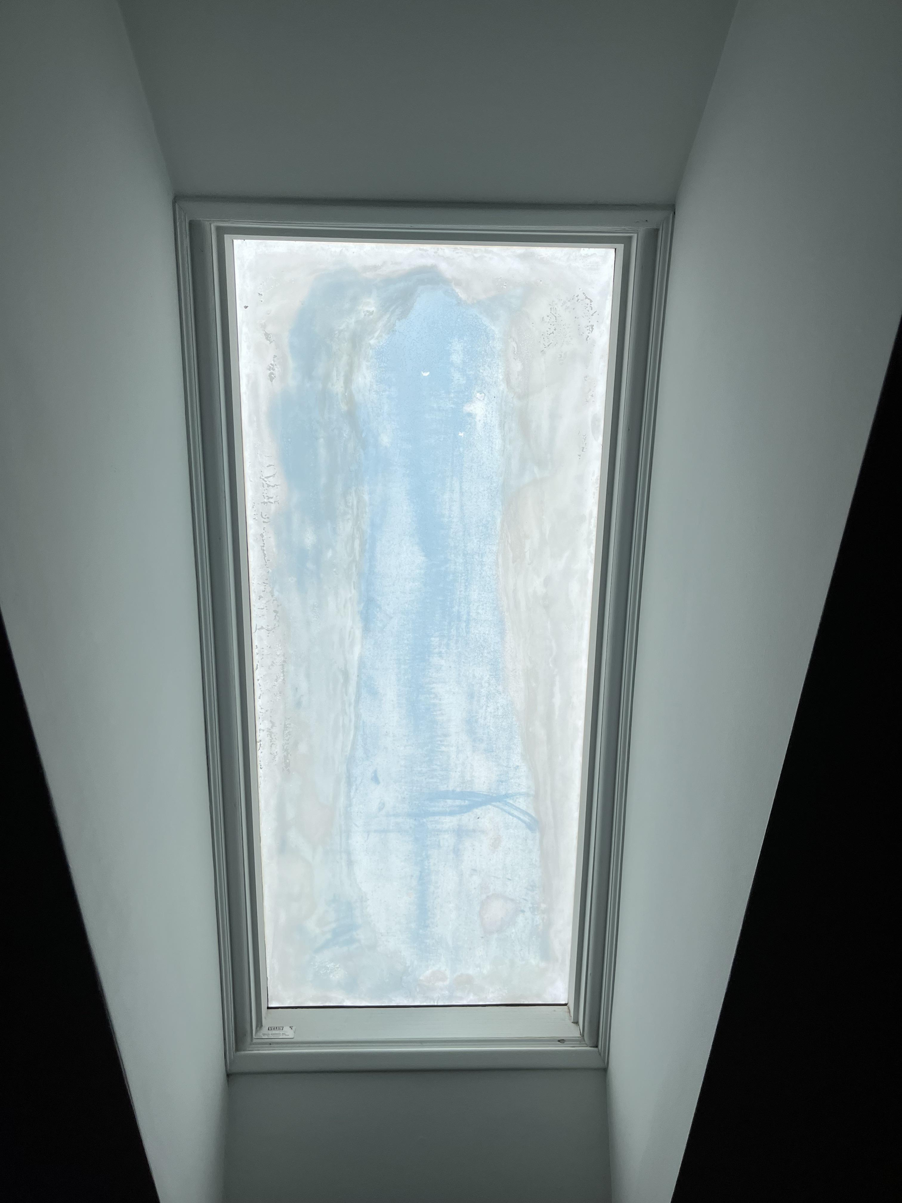 a frostedover skylight is set into a white slanted ceiling.  the skylight shows condensation from top to bottom.  the walls on either side of the skylight are dark.