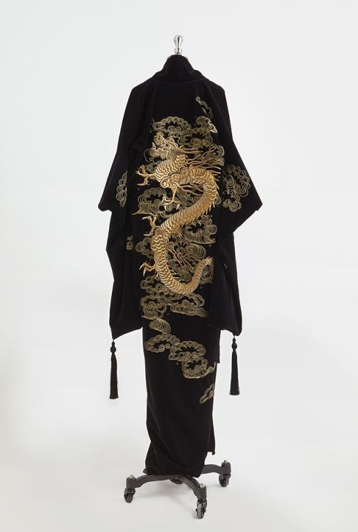 a black kimono with gold embroidery of a dragon and clouds is displayed on a mannequin against a white background. the kimono has wide sleeves and tassels hanging from the edges. the embroidery is detailed and covers a large portion of the back and lower section of the kimono.