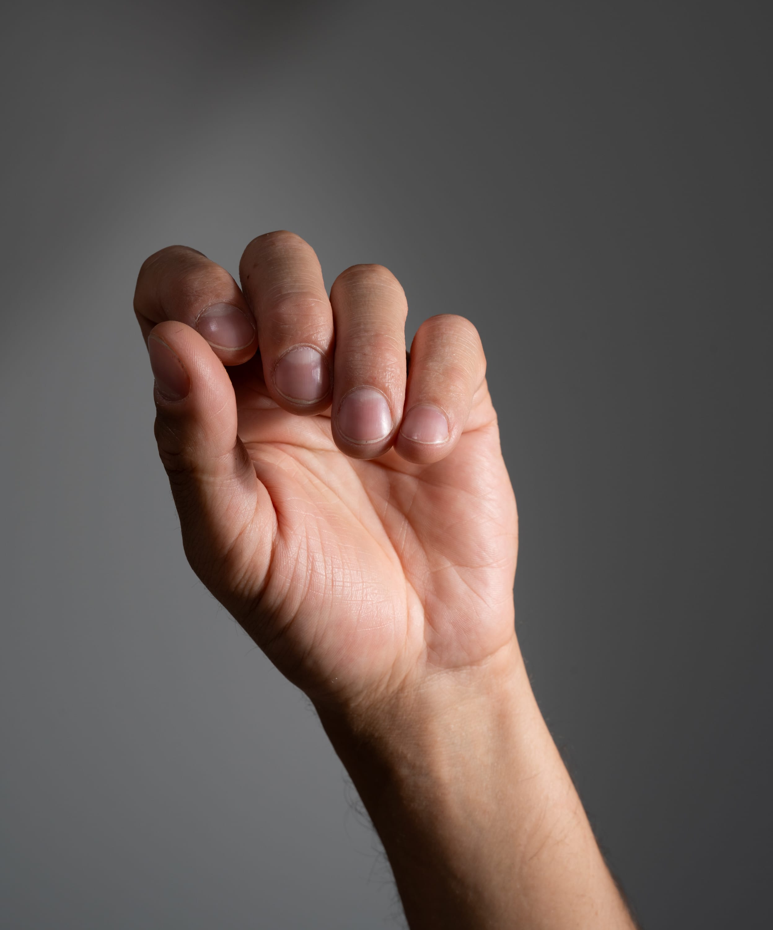 a closeup image of a person's hand subtly clenched with studio lighting against a grey background.