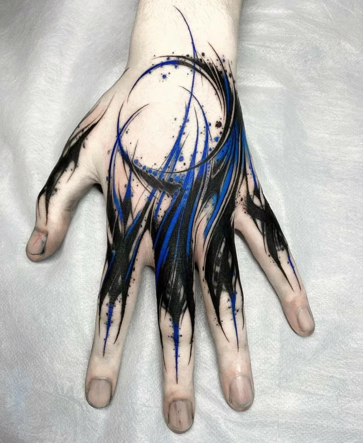 a closeup shot shows a hand with a striking black and blue abstract tattoo design covering the back of the hand and extending onto the fingers. the tattoo features swirling lines and sharp points, creating a dynamic and visually interesting pattern. the combination of black and blue ink gives the tattoo a bold and modern look.