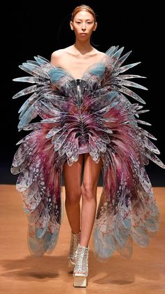 a female model is showcasing a stunning, avantgarde gown on a runway. the dress is a masterpiece of intricate design, featuring a combination of delicate, transparent fabrics, and textures, evoking a sense of lightness and ethereal beauty. the model's poise and the dress's unique construction create a mesmerizing visual spectacle, highlighting the artistic and creative spirit of high fashion.  the model is wearing striking footwear that complements the dress's whimsical nature.