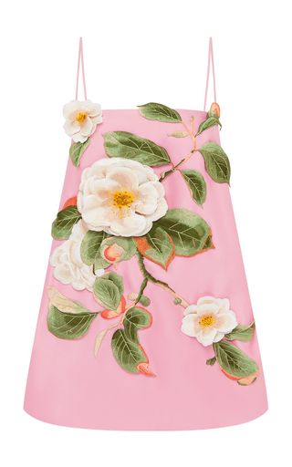a pink sleeveless dress with white flowers and green leaves is displayed. the dress has thin straps and a square neckline, and the floral design features a large white flower in the center and smaller flowers and leaves arranged around it.