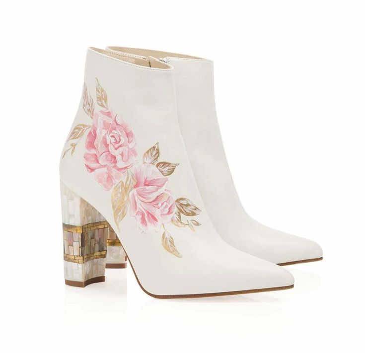 the image features a pair of white ankle boots with a floral design on the side. the boots have a pointed toe and a mosaicstyle block heel. the floral design consists of pink roses and gold leaves. the boots are placed on a white background, creating a clean and minimalist presentation.