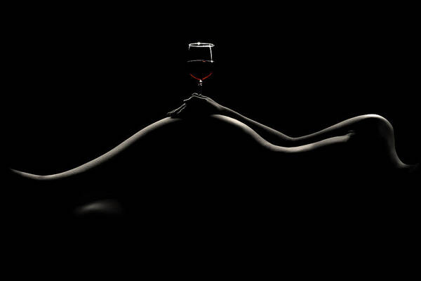 the image is a stark black and white silhouette of a nude woman's body lying down. her form curves gracefully across the frame, creating a flowing, sensual line.  a single glass of red wine rests atop her abdomen, adding a touch of intimacy and intrigue. the high contrast between the dark background and the bright silhouette emphasizes the woman's body, making it the focal point. the overall mood is dark, sensual, and suggestive. the simplicity of the image allows for various interpretations and evokes a sense of mystery and elegance.
