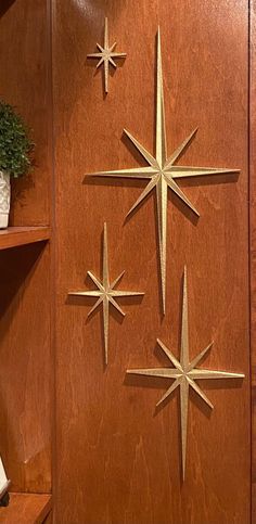 a closeup of a wooden wall panel decorated with four gold stars. the stars are in different sizes and positions. the background is a woodgrain panel. the stars are made of metal and have a retro look to them. the wall panel is likely from a midcentury modern home. the stars add a touch of whimsy and elegance to the space.