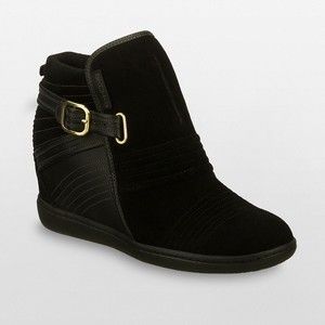 a single black hightop boot with a wedge heel and a gold buckle strap is displayed on a neutral background. the boot has a combination of smooth and textured materials, with horizontal line detailing on both the heel and the toe area. the strap is secured with a goldtoned buckle. the overall style appears modern and fashionable.