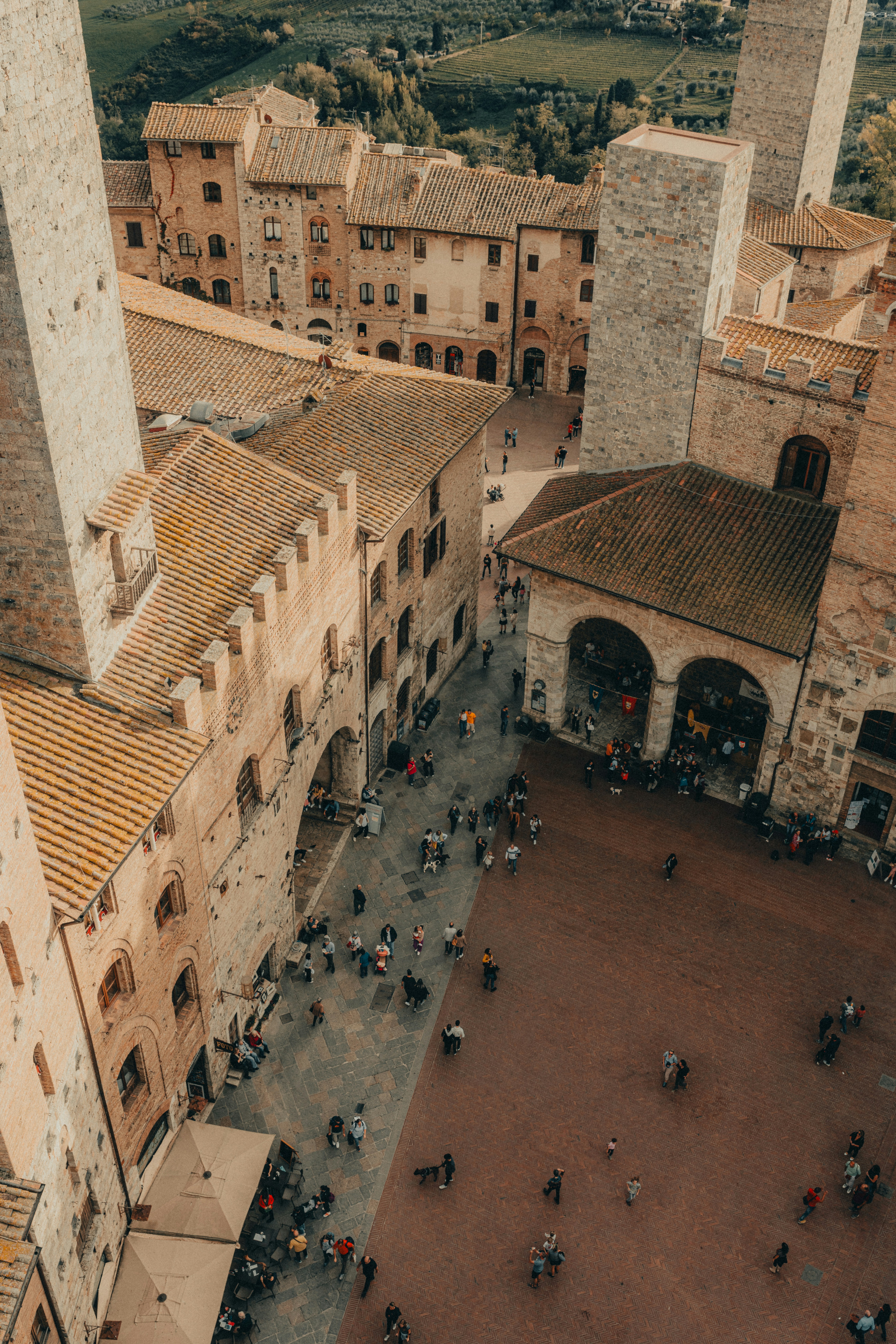 a high angle view of a town square surrounded by old buildings and towers. there are a lot of people walking around the square.