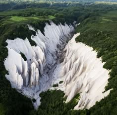 an aerial view of a white rock mountain valley. the valley is carved by erosion, leaving behind a stunning, jagged landscape. the mountain sides are covered in a lush green forest. the image is a breathtaking display of nature's power and beauty.