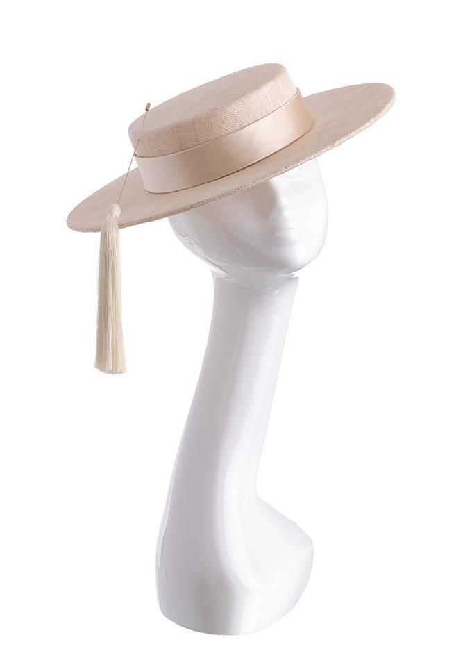 a beige hat with a wide brim and a hatband, it has a white tassel attached to the hatband. the hat is perched on the head of a white mannequin.