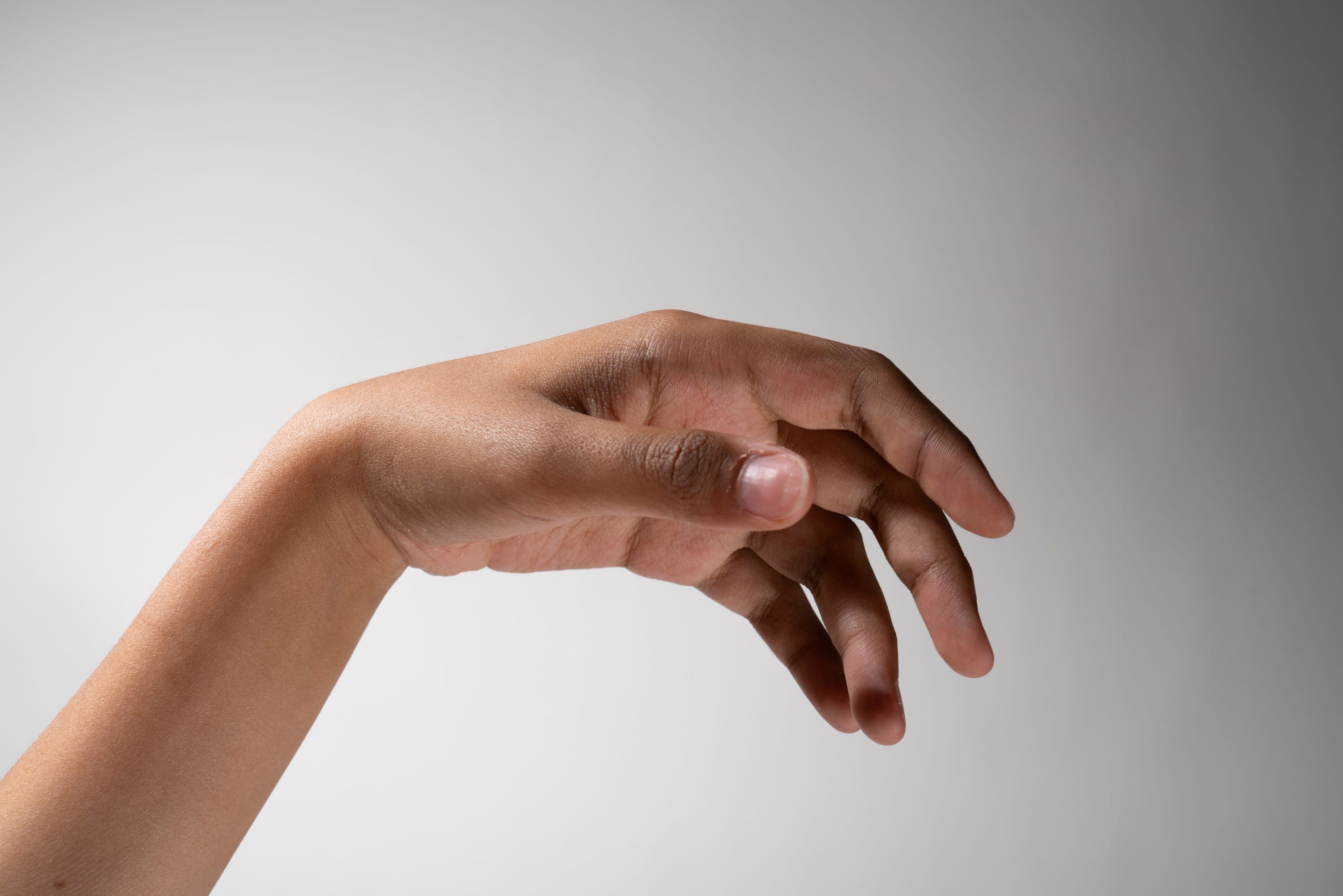 the image shows a hand extended forward with the fingers spread open. it is a closeup shot against a white background. the hand is positioned in such a way that the palm is facing the viewer and the light source is coming from above.