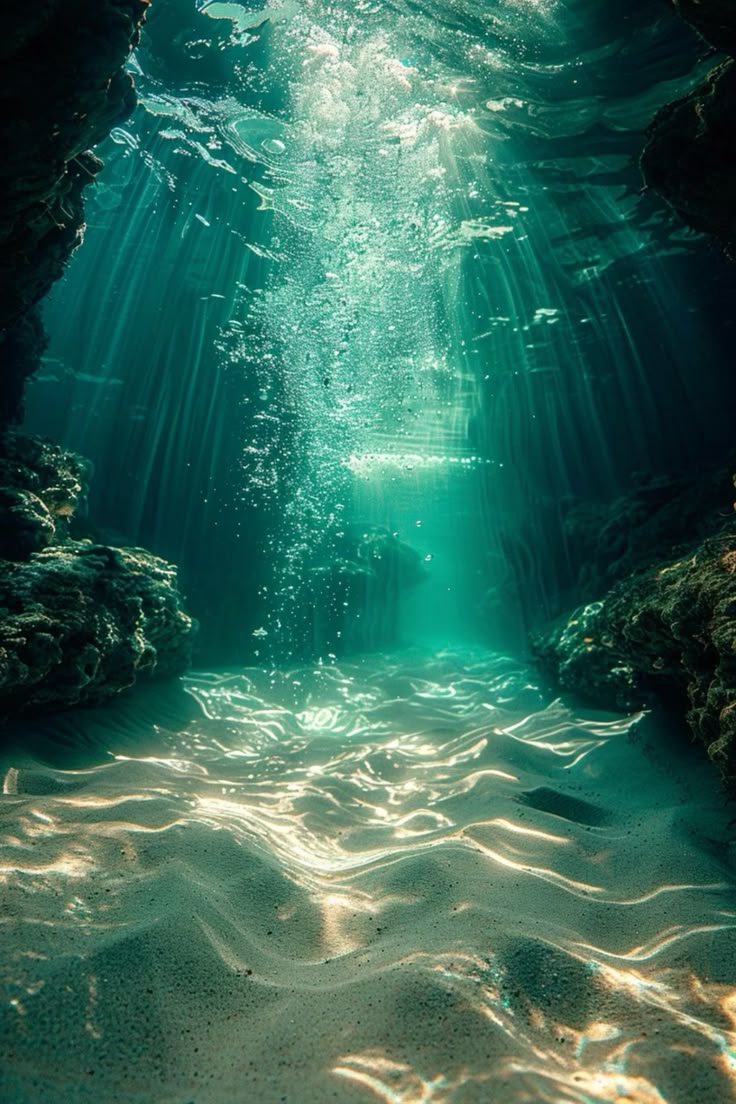 an underwater scene depicting sunlight streaming through turquoise water, creating light rays that illuminate a sandy seabed with visible ripples. bubbles rise towards the surface, and rocks and coral formations flank the sides, suggesting a marine environment possibly near a coral reef.