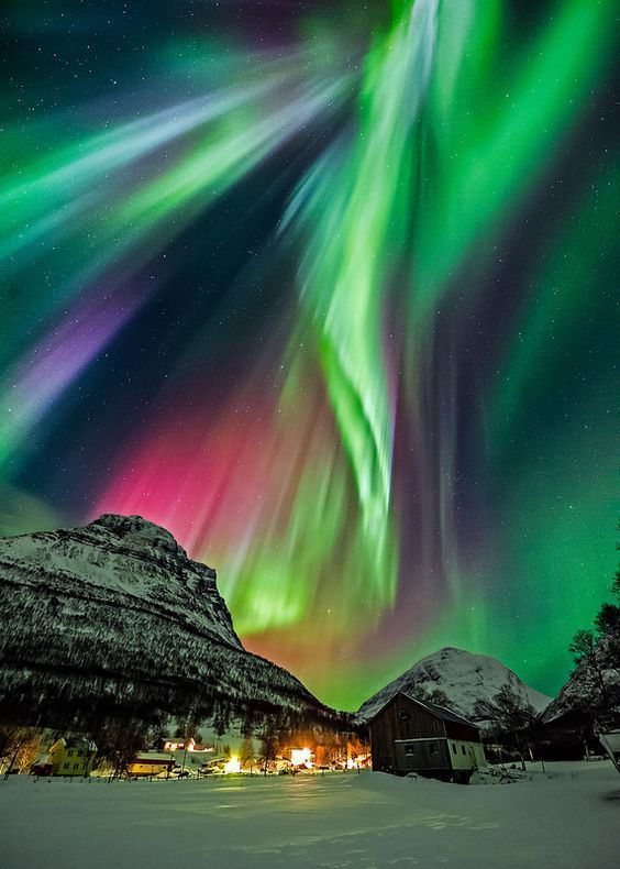 a stunning display of the aurora borealis, or northern lights, illuminates the night sky over a snowcovered landscape. the vibrant green, pink, and purple hues of the auroral curtains dance across the sky, casting a magical glow over the snowcapped mountains and the small town nestled in the valley. the starry sky adds to the sense of wonder and beauty of this scene.
