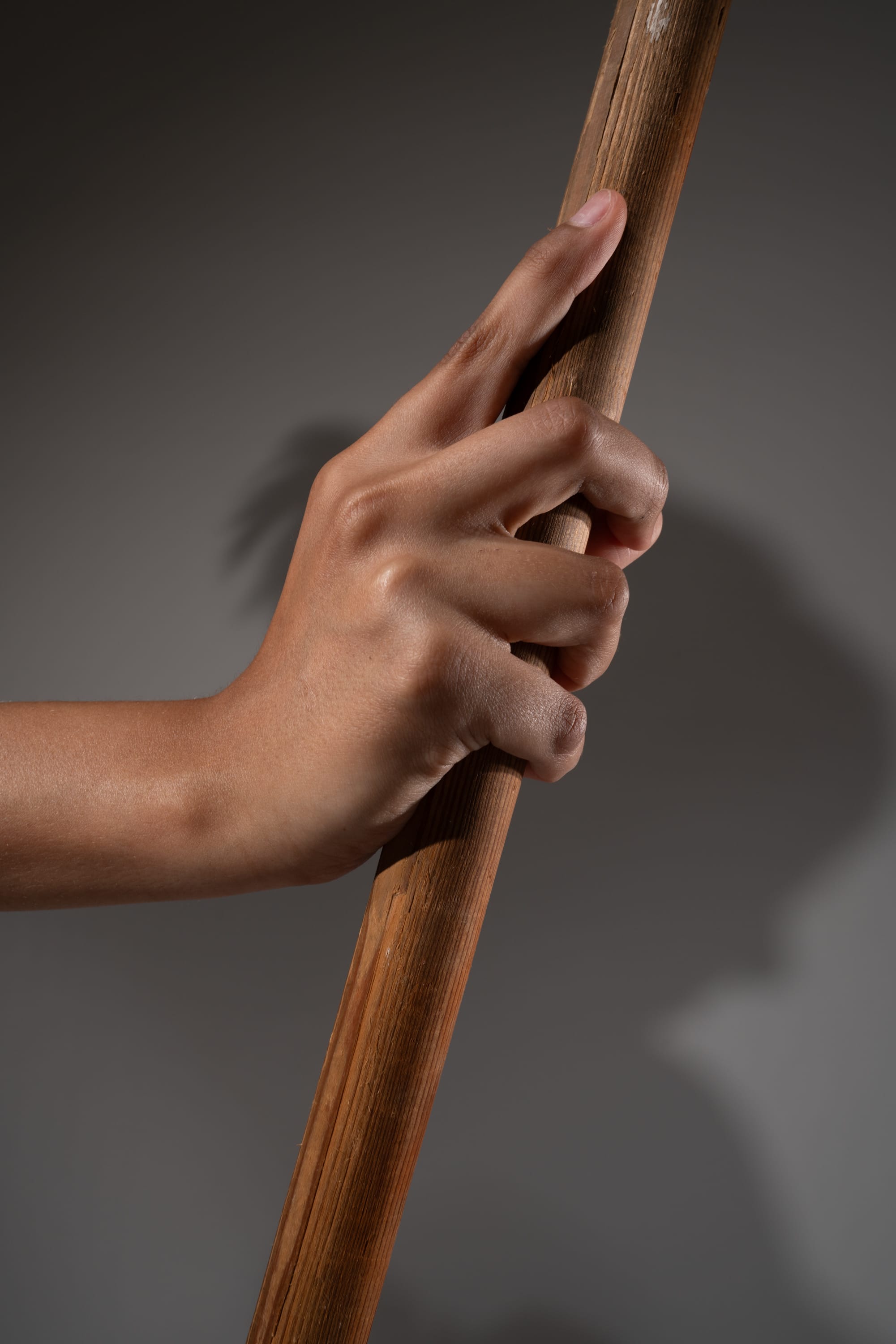 a closeup image of a hand gripping a wooden stick. the hand is illuminated with studio lighting, creating a strong shadow on the background. the texture of the wood and the details of the hand are clearly visible.