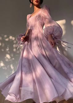 a young woman in a flowing purple dress poses gracefully. the dress is sheer and delicate, with soft, romantic details like puffed sleeves and a slightly gathered neckline. the light catches the fabric beautifully, creating a dreamy and ethereal atmosphere. the woman's expression is soft and gentle, and she seems to be lost in thought. overall, the image is elegant, feminine, and romantic.