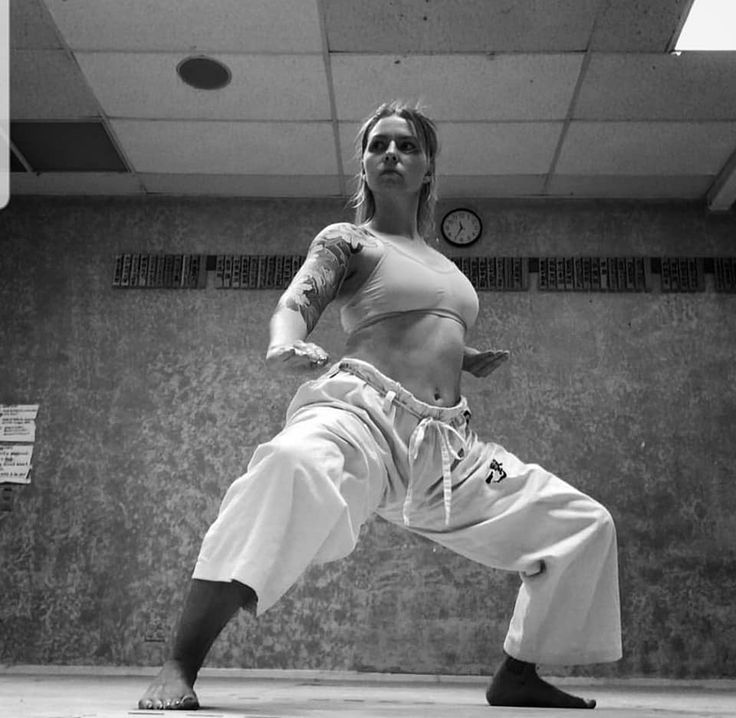 a woman in a white karate uniform, standing in a fighting stance, looking determined and ready to fight. the image is black and white, giving it a classic and powerful feel. the woman's muscles are tense, and she is focused on her opponent, ready to strike at any moment. she is a true martial artist, strong and powerful.