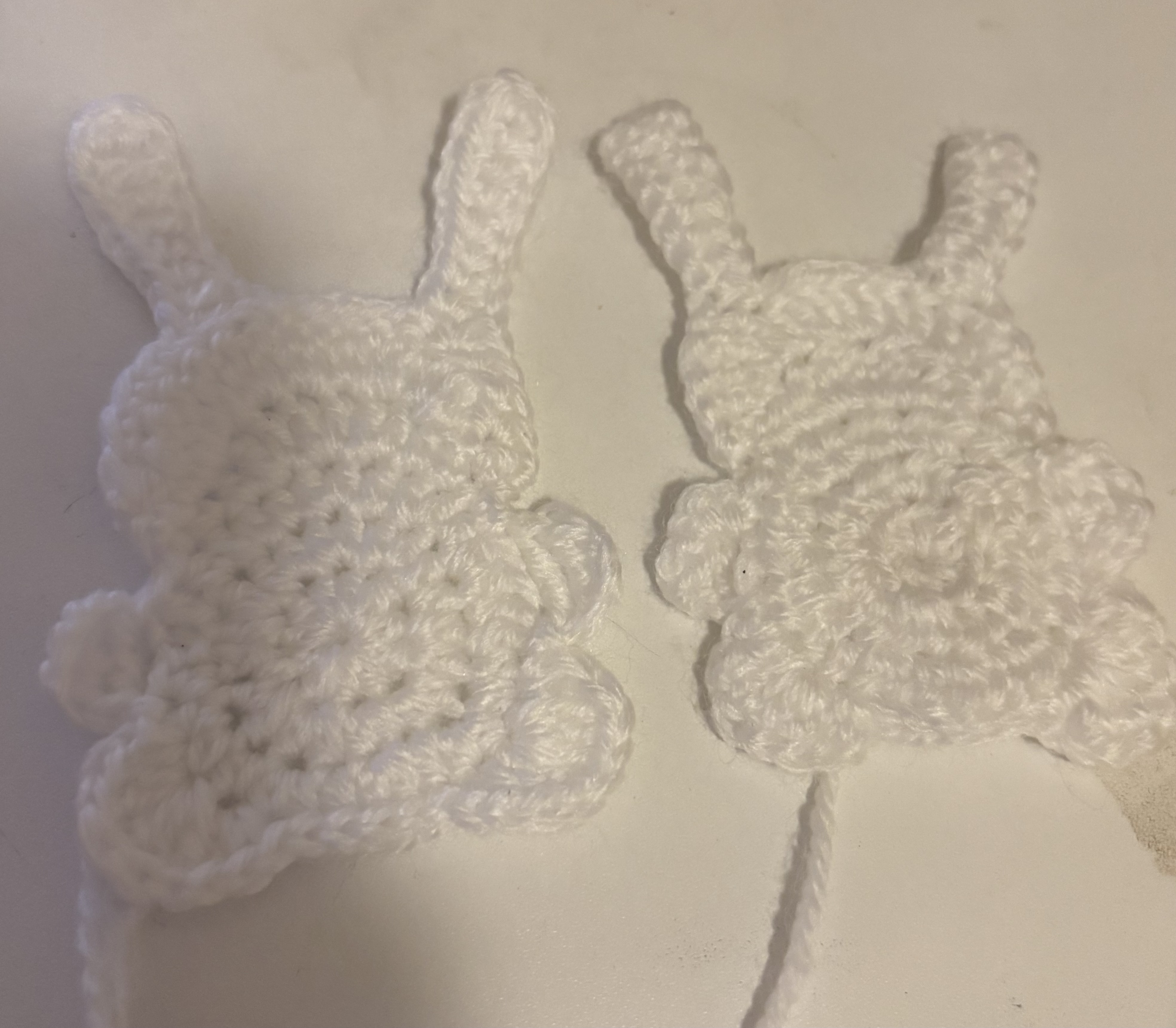 two white crochet bunny decorations are laying on a white surface.