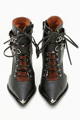 a pair of black leather women's ankle boots with pointed toes are shown in the image. the boots are laceup style with buckles and cutouts.  they have a slightly western or goth aesthetic with metal studs at the toe.  the boots are shown from a slightly elevated angle, with the toes pointed towards the bottom of the image. the interior of the boots is a contrasting light brown color.