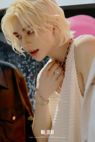 a portrait of a young asian man with long blonde hair. he is wearing a white tank top and jewelry. he is looking at the camera with a serious expression.