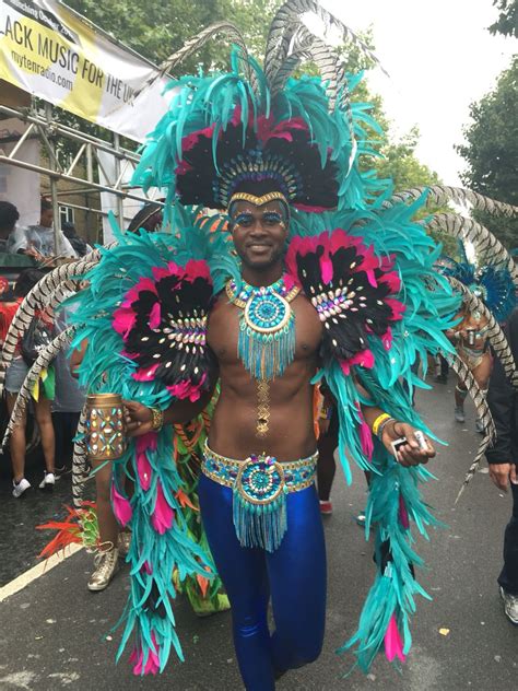 a man in a vibrant and colorful costume, adorned with feathers, is captured in the middle of a bustling carnival parade.  he is smiling and radiating joy, showcasing the energy and spirit of the event. the bright colors, intricate details of his costume, and the festive atmosphere around him create a captivating and exciting visual.