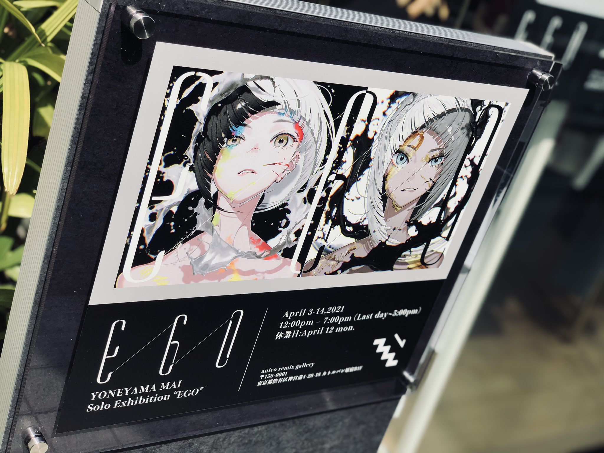 a sign advertising a solo art exhibition by yoneyama mai titled "ego". the sign features an illustration of two female characters with black and white hair and colorful accents. the exhibition runs from april 3rd to 14th, 2021.
