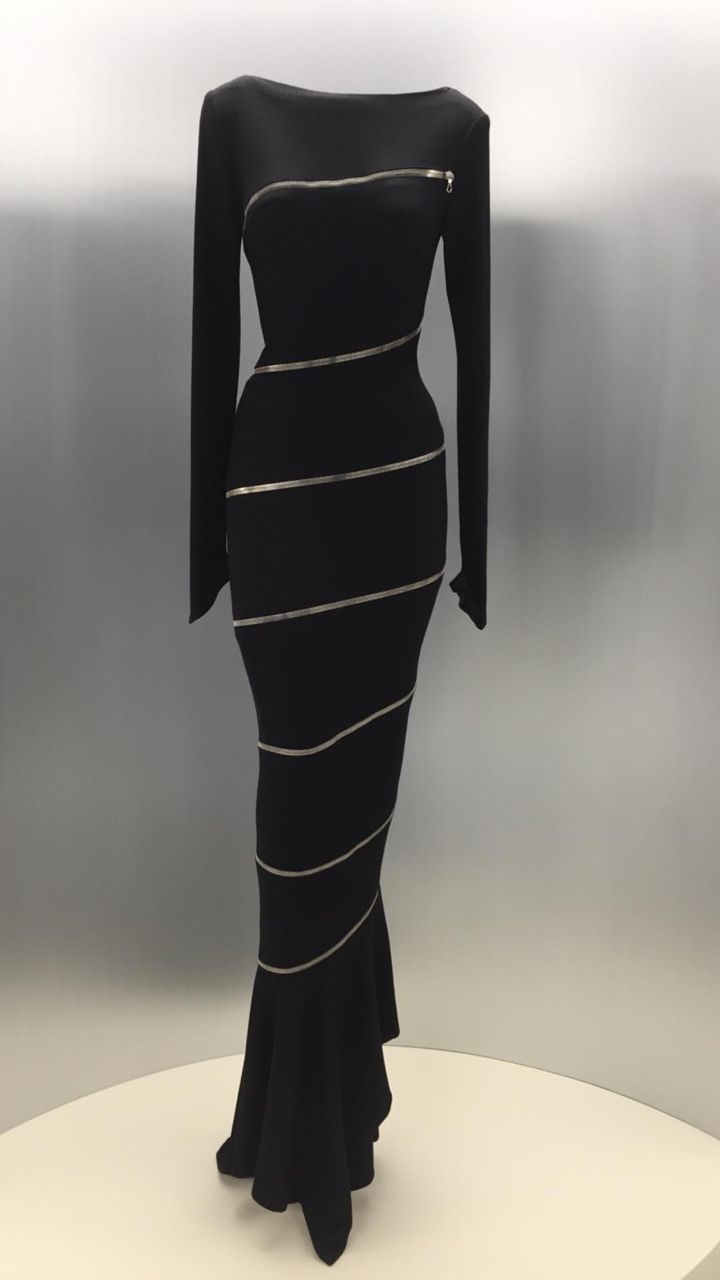 a long black dress with a mermaid tail, featuring a series of diagonally running zippers. it has long sleeves and a boat neckline.