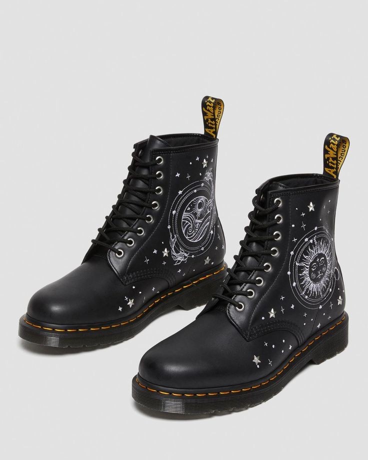 a pair of black dr. martens 1460 boots with white celestial embroidery, including stars, a moon, and a sun. the boots are laceup and have a classic dr. martens silhouette. the boots are sitting on a white background.