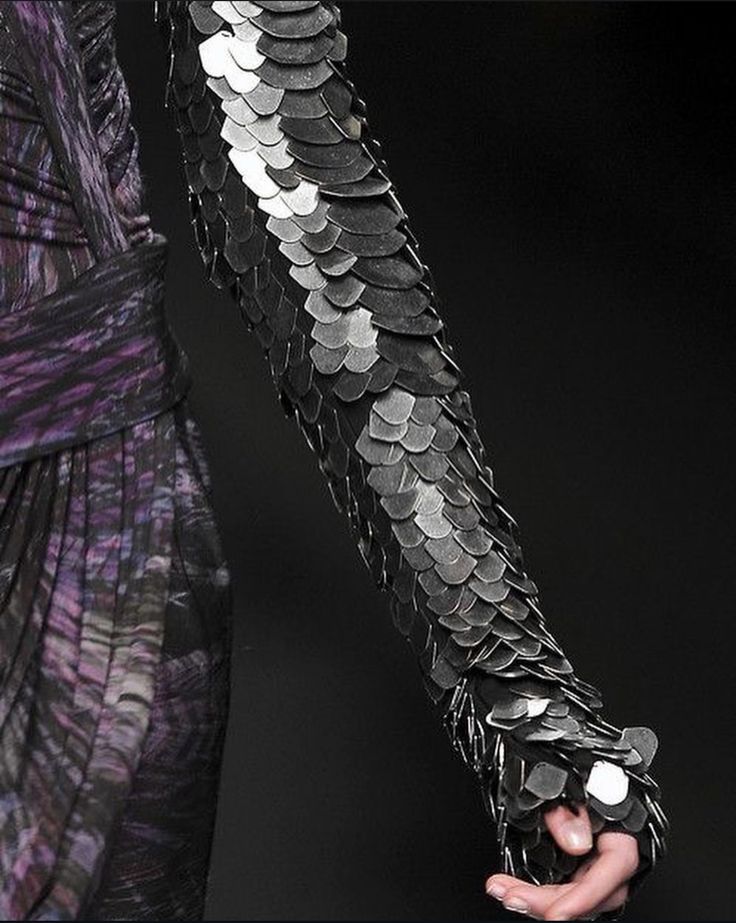 a closeup shot of a model's arm adorned with a striking black and silver sequined sleeve. the intricate design resembles scales, creating a dramatic and futuristic effect. the sleeve extends onto the hand, adding a touch of glamour and edginess to the overall look. the background is a blurred black, emphasizing the intricate details of the sleeve.