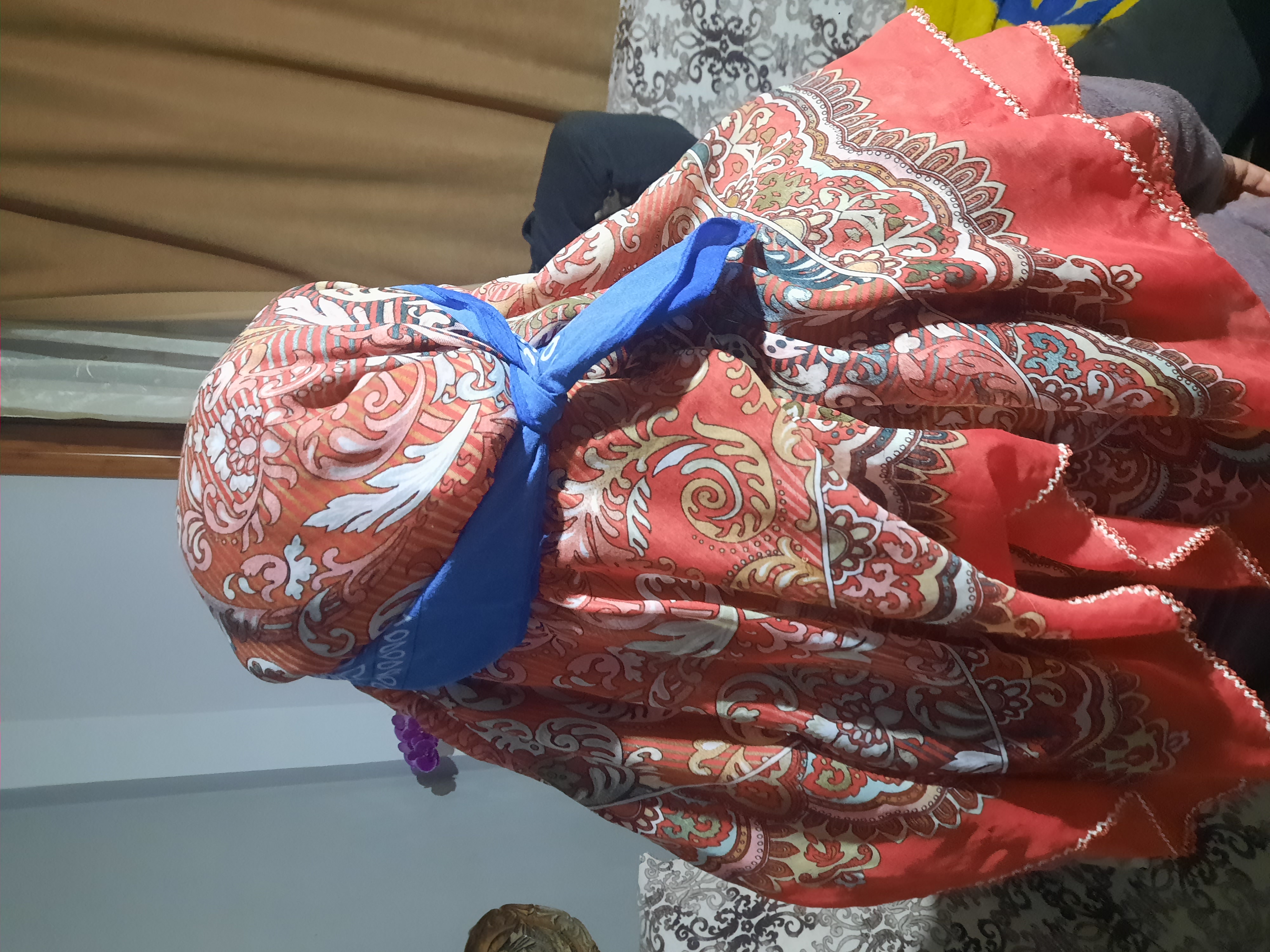 a person is covered in a red and orange patterned headscarf secured with a blue ribbon.