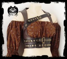 a woman models a brown steampunkinspired leather vest with multiple buckles and straps. the vest is worn over a matching brown brocade blouse with puffed sleeves. the background is a dark, textured surface, and the lighting is bright, highlighting the details of the clothing.