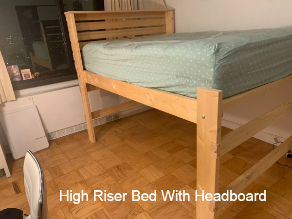 a wooden high riser bed with a headboard. the bed has a light wood finish and is raised off the ground, with space underneath for storage or other furniture. the bed is covered with a light green sheet with white polka dots. the room has parquet flooring and a window.