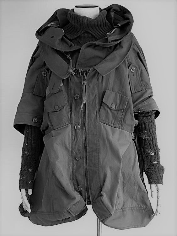 black and white studio shot of a deconstructed, avantgarde jacket on a mannequin. the jacket is dark grey with multiple layers, pockets, buttons and a zipper. it has a large hood and the sleeves are layered with what appear to be distressed knit fabric. the overall style is grungeinspired and highfashion. the mannequin is simple and does not detract from the garment. the background is plain white, further emphasizing the jacket.