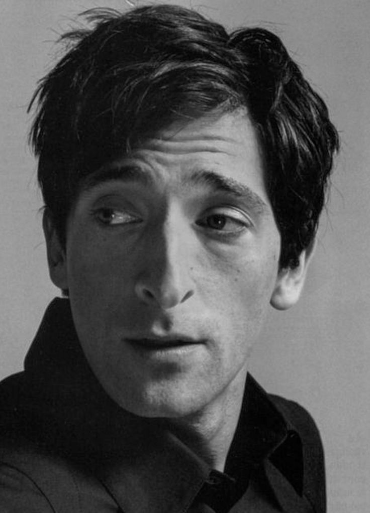 a black and white portrait of actor adrien brody, showing his head and shoulders. he is wearing a dark shirt and looking slightly off to the side.