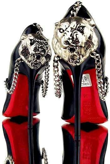 a pair of black stiletto high heels with red bottoms and silver animal print accents. the heels are adorned with silver chains and have a distinctive edgy design. the shoes are presented in a classic fashion photography style, showcasing their detail and elegance.