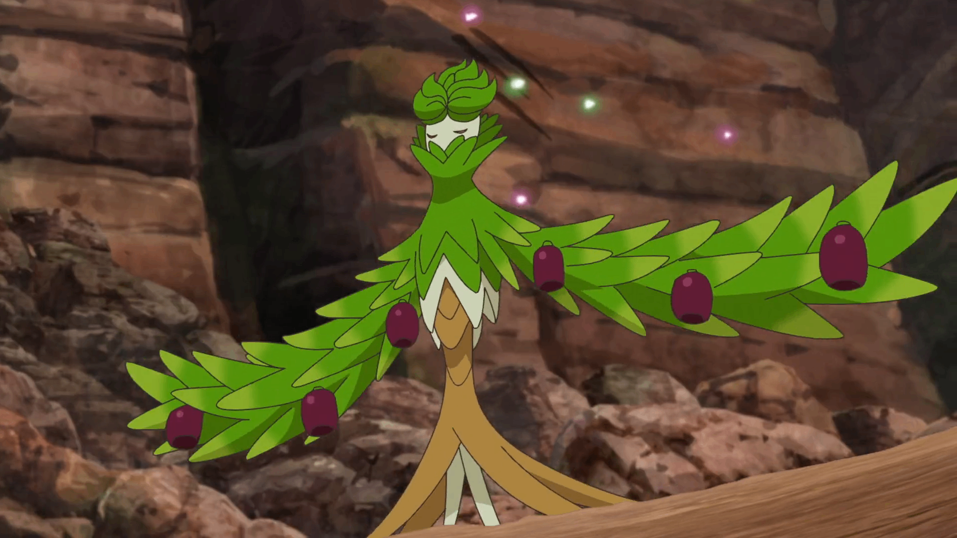 a closeup shot of a pokémon, possibly a evolved form of sprigatito, standing on a log. the pokémon is predominantly green and brown, with leaves and purple berries adorning its body. it has a plantlike appearance with a humanoidlike structure. the background features rough rocks and a dimly lit environment, suggesting a cave or rocky terrain.  small, glowing particles are visible around the creature, adding a magical or mystical element to the scene. the style is consistent with pokémon animation.