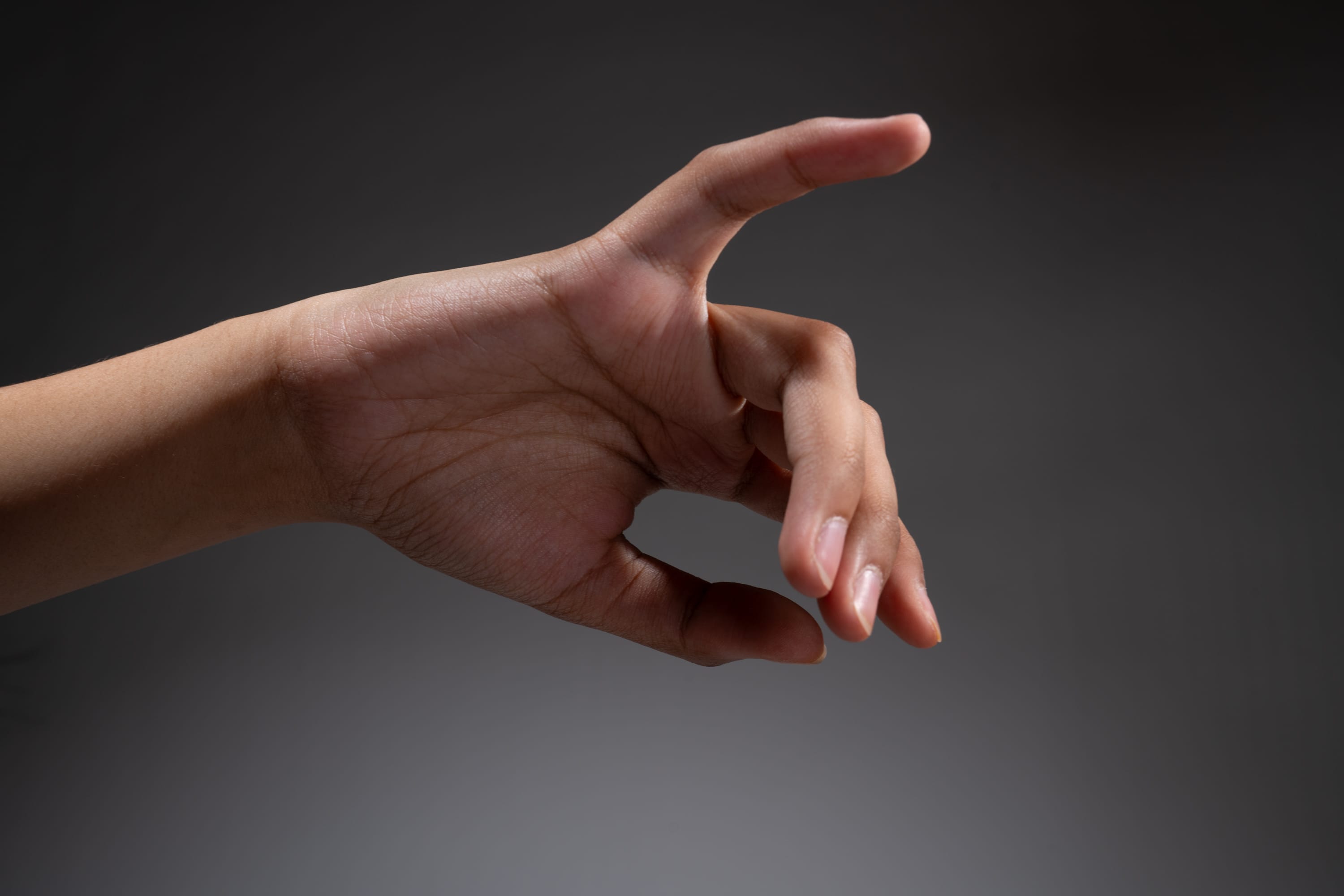 a hand is reaching out against a gray background, with the index finger and thumb forming a pinching gesture as if about to grab something.