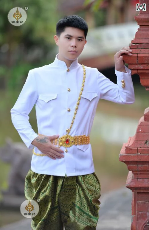 a handsome man in a white traditional thai wedding outfit,  with gold trim and a green sarong. he is smiling and looking at the camera. he is standing in front of a brick wall with a goldtrimmed roof. the man looks very happy and excited for his big day.