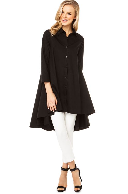 a full shot features a fairskinned woman with blonde hair in a highlow black shirt dress, white pants and black high heeled shoes standing on a white background.