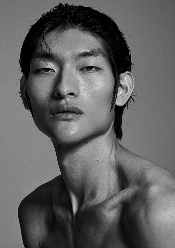 a striking black and white portrait of a young asian man with a sleek, wet hairstyle. he is bareshouldered, emphasizing his neck and jawline. the lighting highlights the contours of his face, giving the image a dramatic and artistic feel.