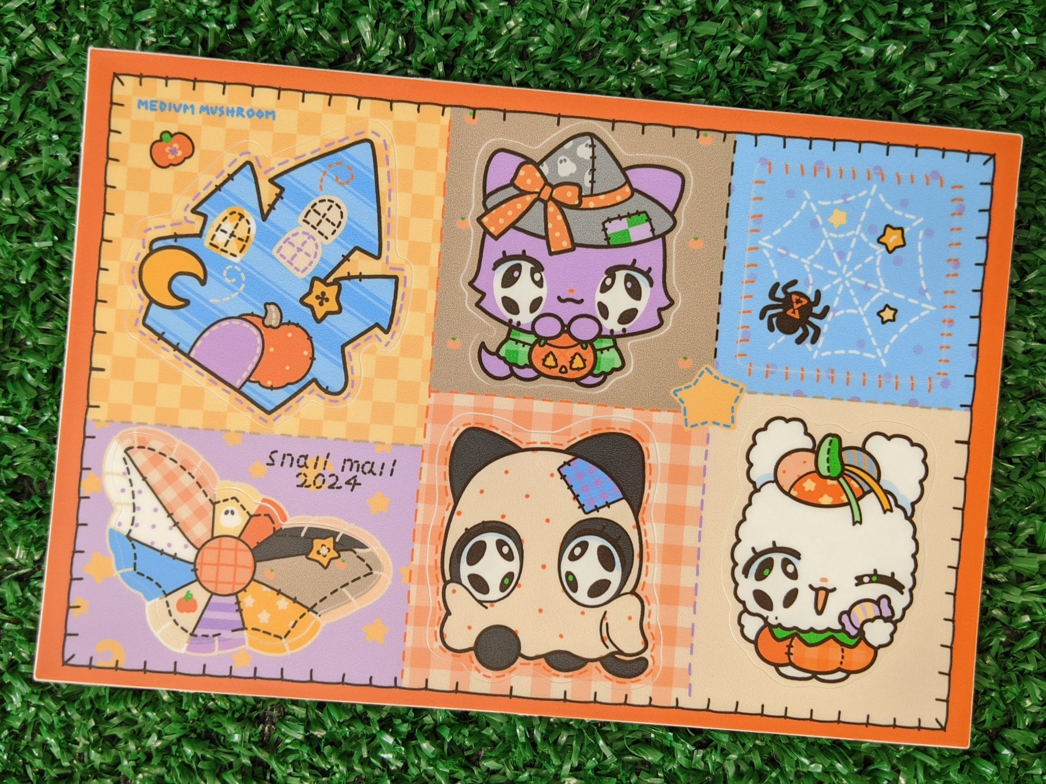a closeup shot of a halloweenthemed sticker sheet. the sheet features a patchwork design with various cute characters, including a witch cat, ghost panda, bunny, and a haunted house. the overall style is kawaii and pasteltoned.  the sticker sheet is on a green surface. the text "snail mail 2024" and "medium mushroom" are visible on the sheet.