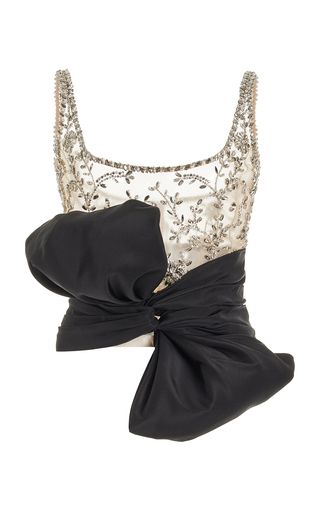 a sleeveless white top with silver floral beading and a large black bow on the left side. the top has a square neckline and the bow is tied at the waist.