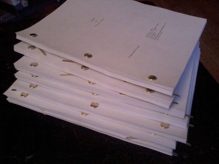 this image shows a stack of screenplays or film scripts. the scripts are bound together with brass fasteners, also known as brads. they are neatly stacked, suggesting a completed or readytobeused manuscript.