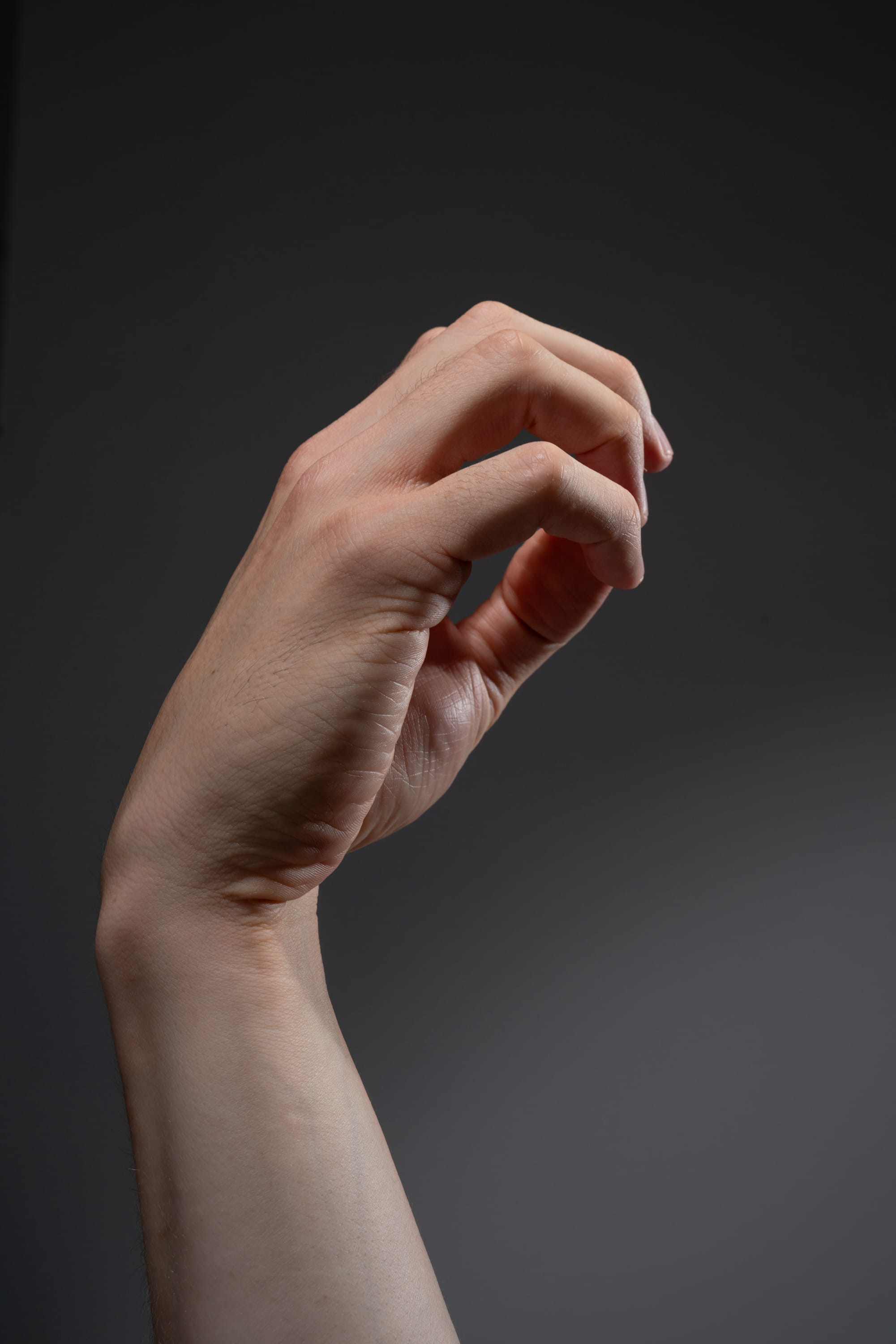 a closeup image of a hand against a gray background. the hand is in a grasping gesture with the fingers curled inward. the lighting is bright, highlighting the details and texture of the skin.