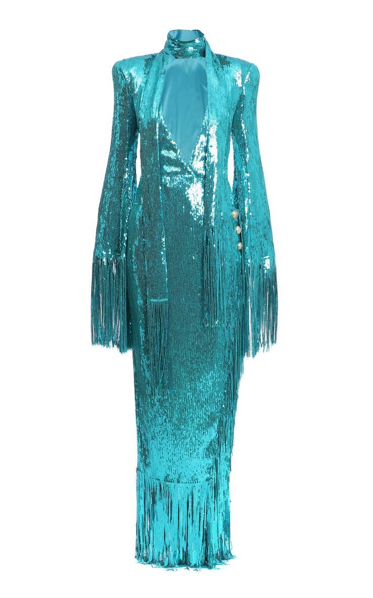 a long turquoise sequin dress with fringe details on the sleeves and hem. the dress has long sleeves, a high neckline, and decorative buttons on the upper arm. the dress also has a partial open chest covered with the same fabric in a similar turquoise tone.