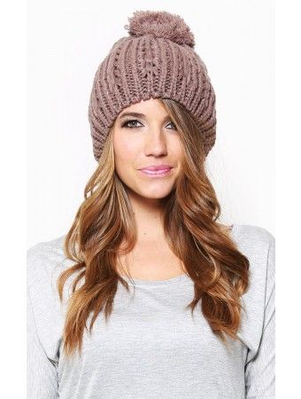 a young woman with long brown hair is wearing a grey beanie with a pom pom. she is wearing a grey top and has a beautiful smile on her face. she looks happy and confident.