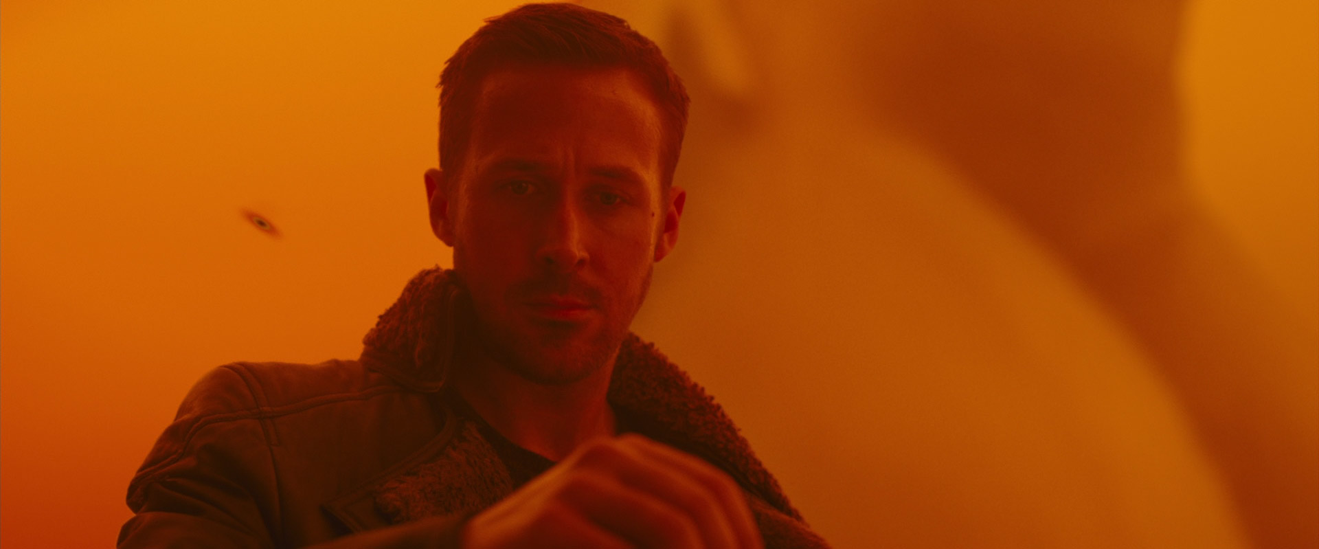 ryan gosling as officer k in a scene from blade runner 2049. the image is dominated by a warm orange hue, creating a futuristic and dystopian atmosphere. gosling's intense expression adds to the suspenseful mood.