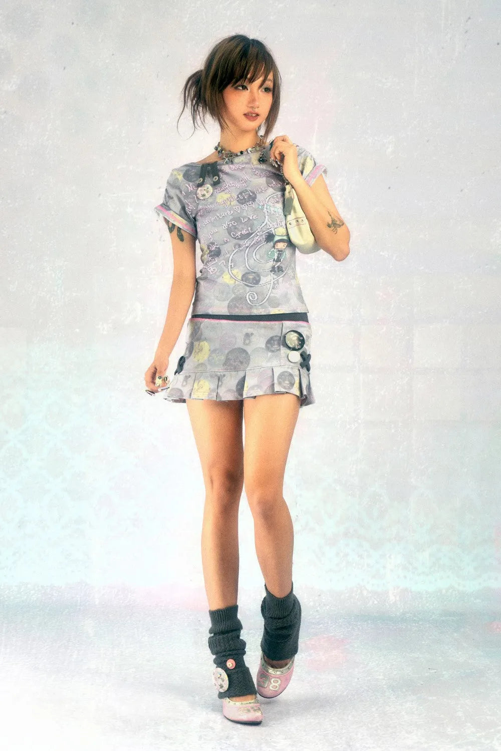 a young asian woman with short brown hair is posing in a studio against a lightgrey background. she is wearing a shortsleeved grey and white patterned dress with a pleated skirt, dark grey leg warmers, and light pink shoes. she is carrying a light grey handbag over her shoulder. the overall style is cute and trendy, with a slight hint of a japanese fashion influence.