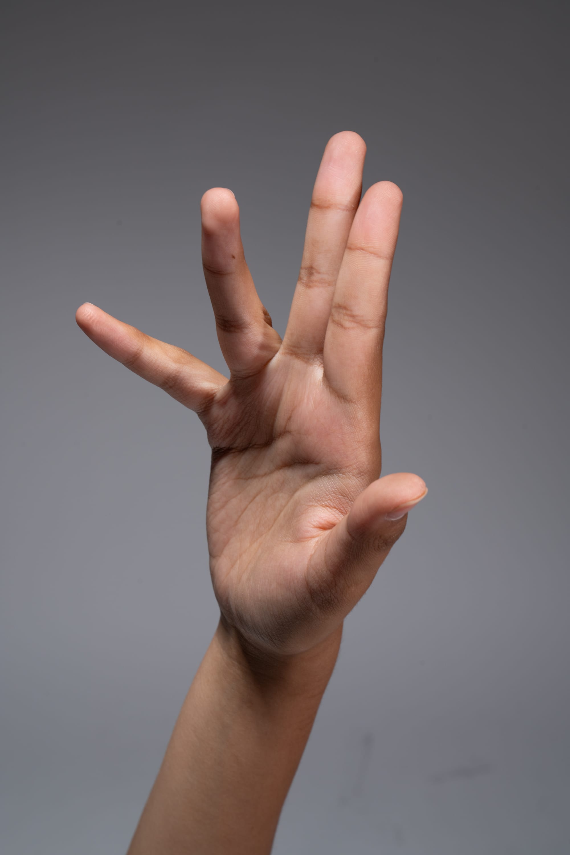 a hand is held up against a gray background with the index, middle, and ring finger extended and spread apart. the pinky finger is curled in towards the palm.  the thumb is also extended and apart from the index finger. the hand is positioned so that the palm is facing the viewer.