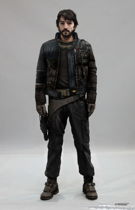 a man stands looking at the camera with his arms down by his side. he's wearing a black leather jacket, dark jeans, and dark boots. he's holding a gun with his right hand. the background is a plain grey color.