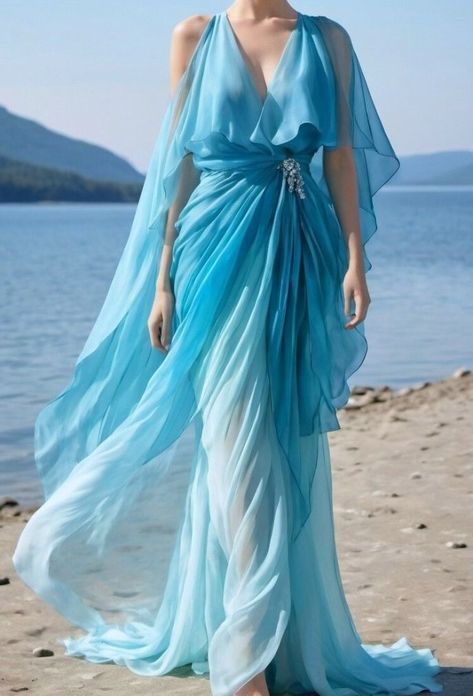 a woman in a flowing, ombre blue chiffon gown stands on a sandy beach. the dress is a light, airy fabric that moves gracefully with the breeze. the woman's hair is loose and wavy, and she is wearing a delicate silver necklace. she looks beautiful and confident in her dress. the sun is shining and the sky is blue, creating a dreamy and romantic atmosphere.