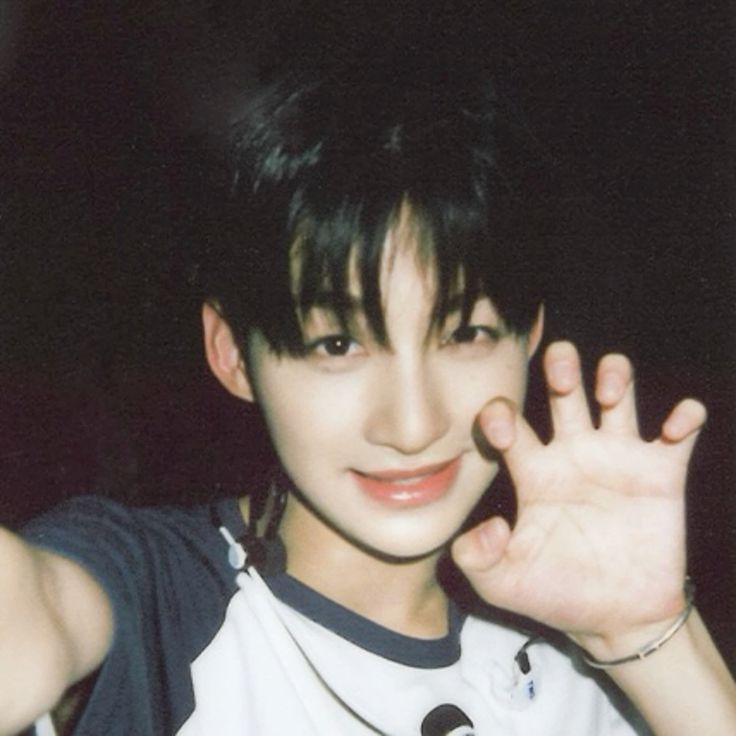 a portrait of a young asian man smiling, he is wearing a white and blue shirt and has black hair. he appears to be happy and in a good mood. the photo was taken with a film camera, creating a vintage look.